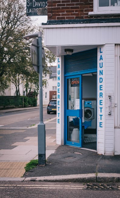 A black wheeled rubbish bin labeled 'ST. JOHN'S' is positioned on the edge of a street at night, with its lid open revealing discarded cardboard boxes, paper, and miscellaneous debris inside. The bin
